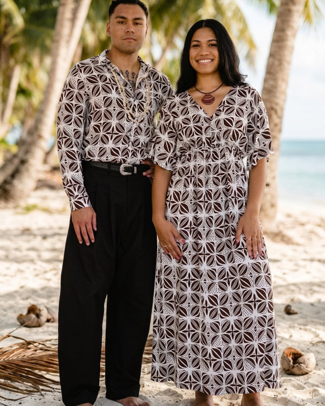 Man and woman in matching patterned outfits standing on a beach with palm trees in the background.