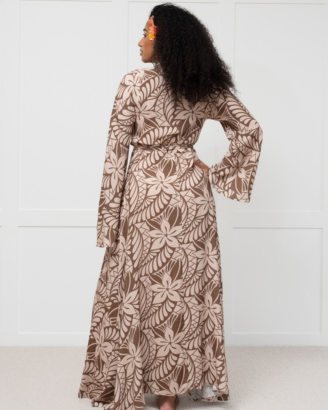 Woman wearing a long brown floral island dress against a white background