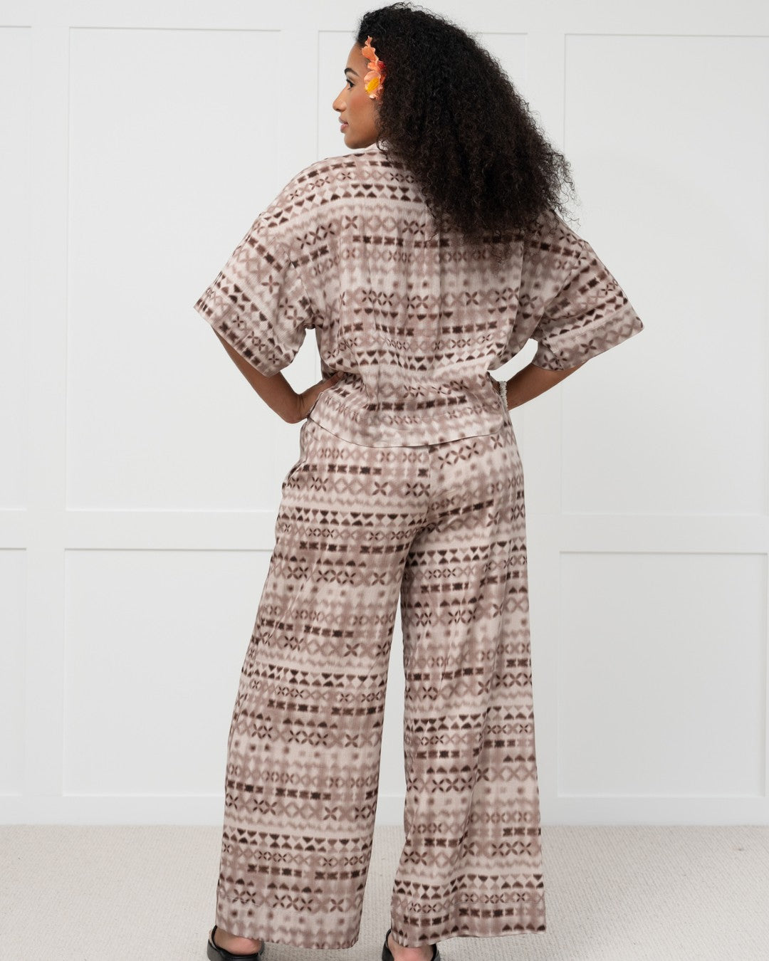 Woman wearing a patterned outfit with wide-leg island pants and shirt set against a white background