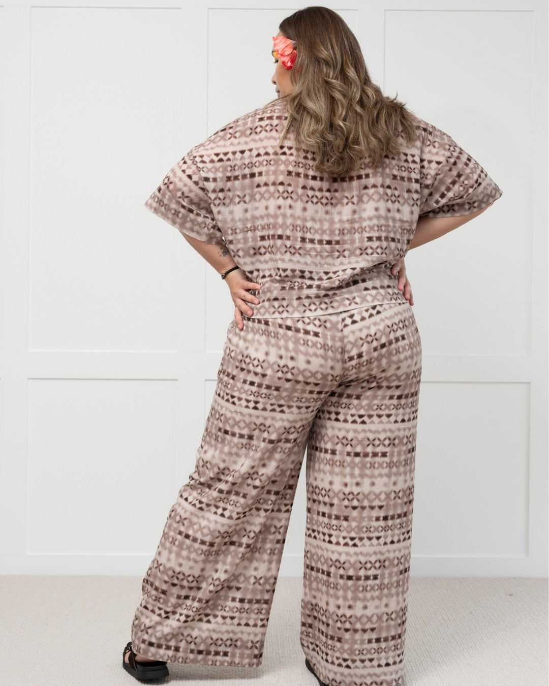 Woman wearing a patterned outfit with wide-leg island pants and shirt set against a white background