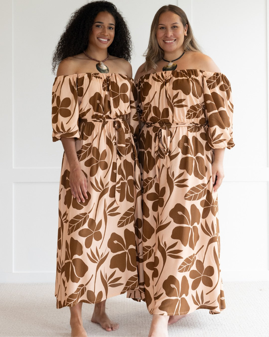 Woman wearing a floral off-shoulder island dress against a white wall.
