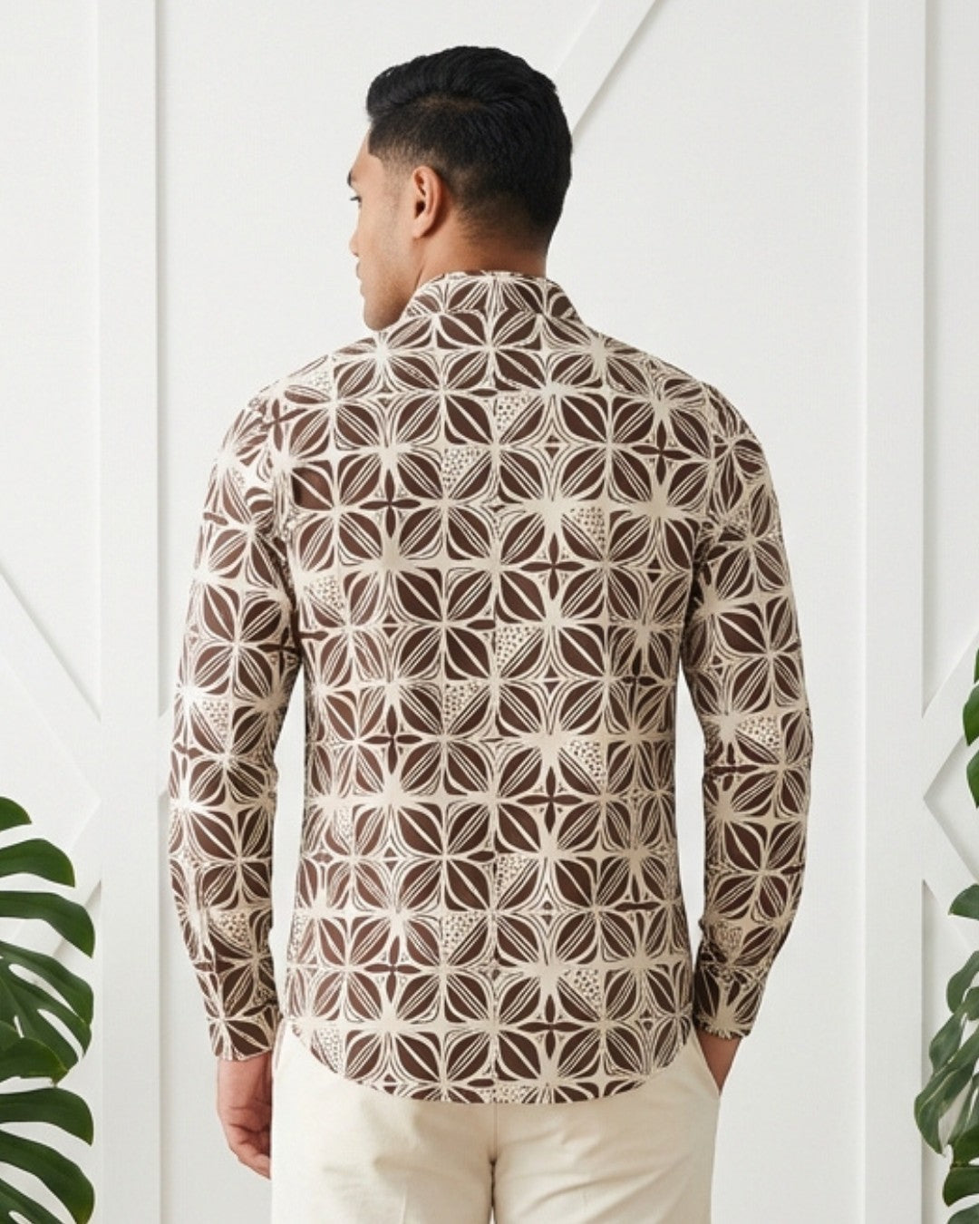 Man wearing a patterned shirt standing against a white paneled wall.