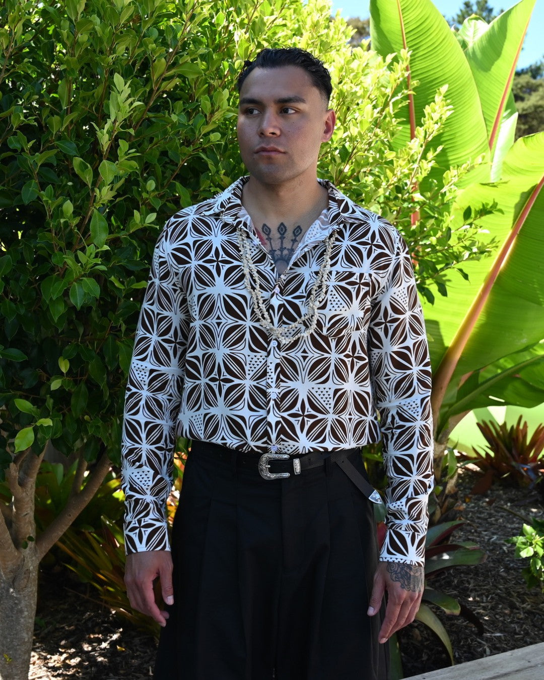 Man wearing a patterned island shirt and black pants standing in a garden