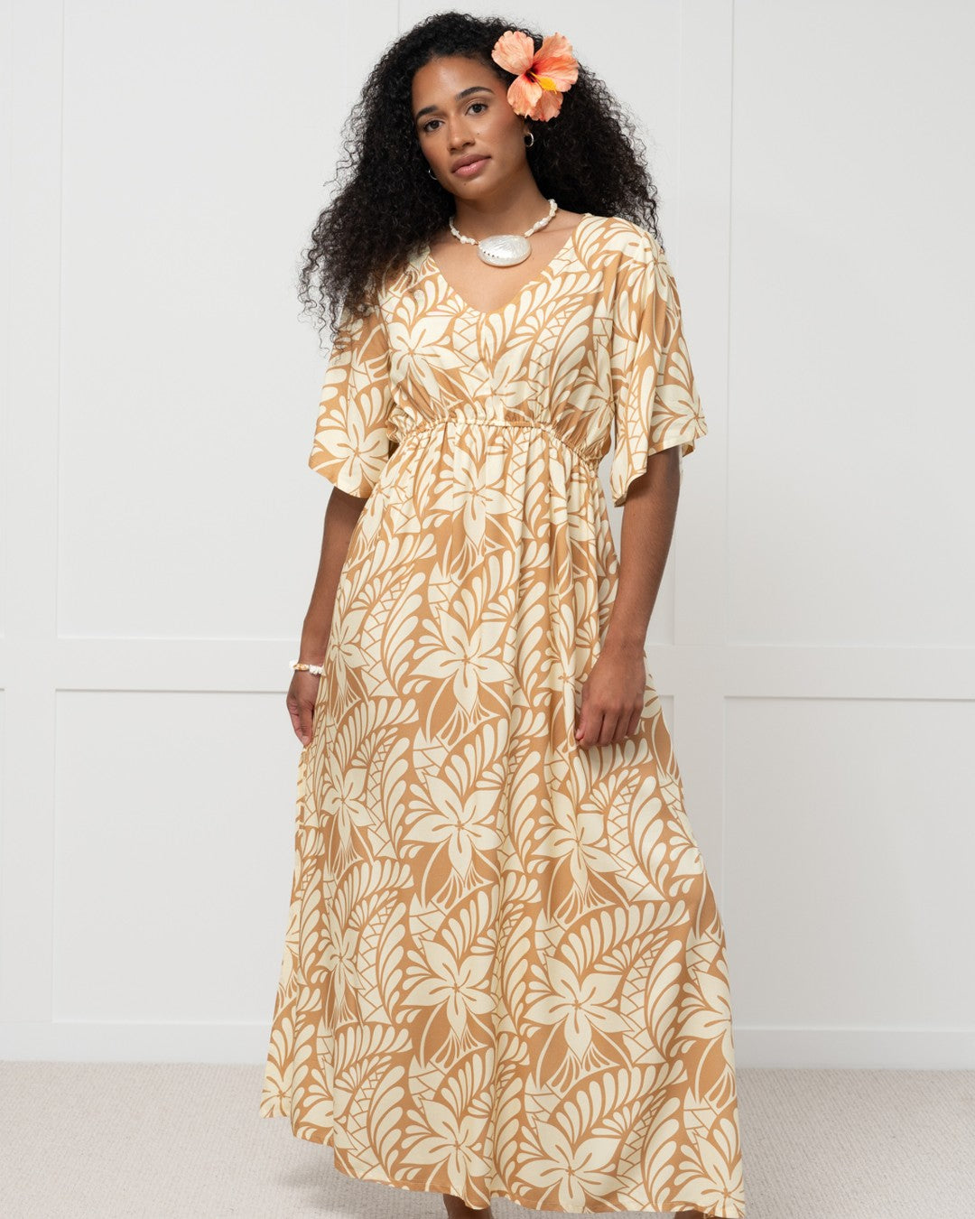 Woman wearing a long, patterned island dress against a white background