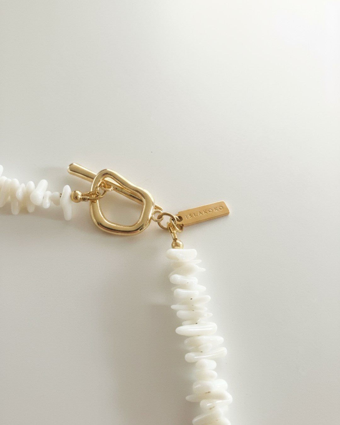 Necklace with gold clasp and white beads on a light background
