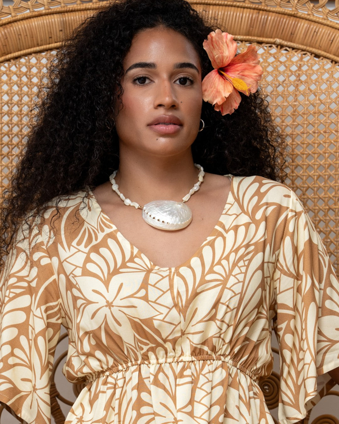 Woman wearing a patterned dress with a floral headpiece, sitting on a wicker chair.