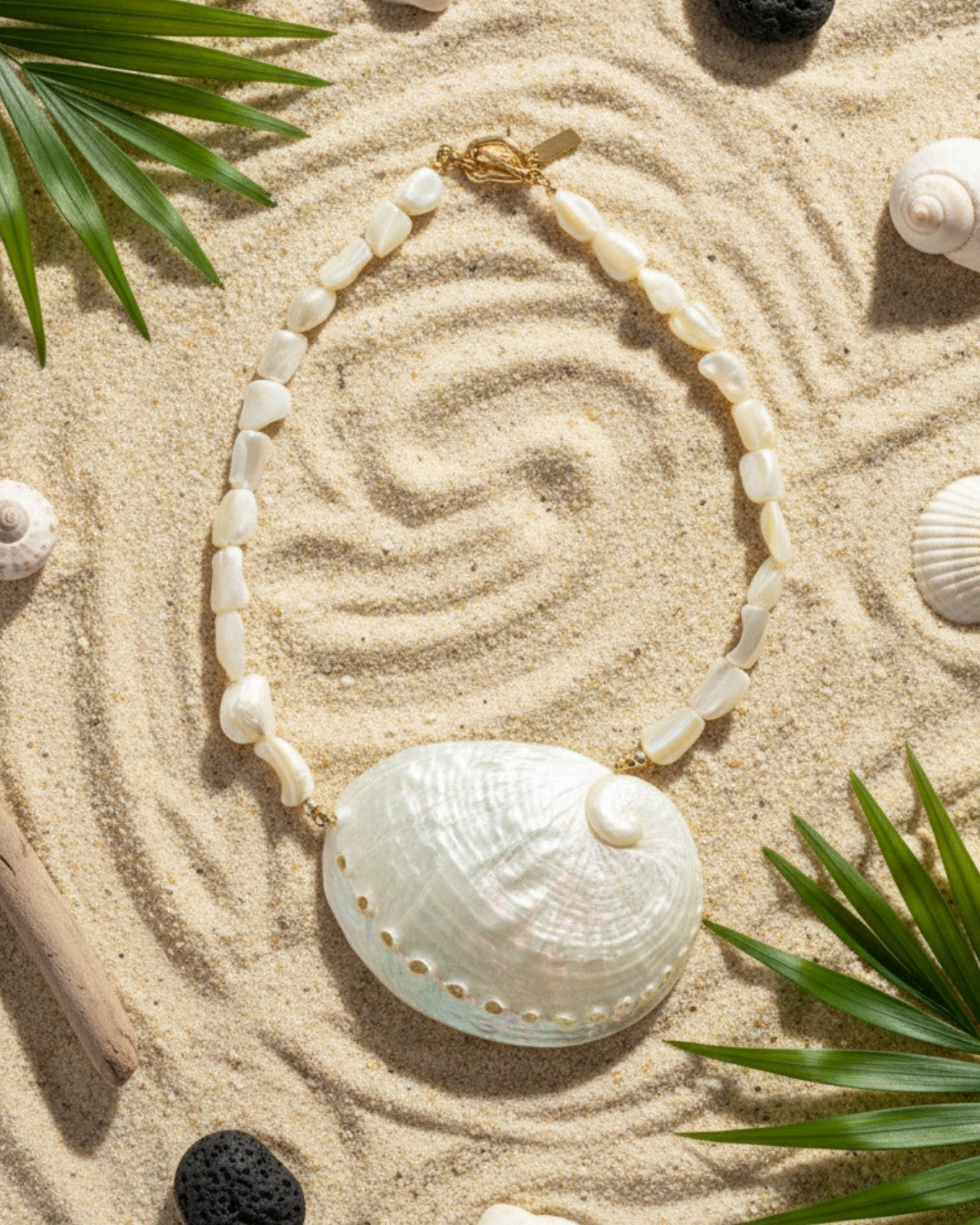 Necklace with a shell pendant on sand surrounded by leaves and shells