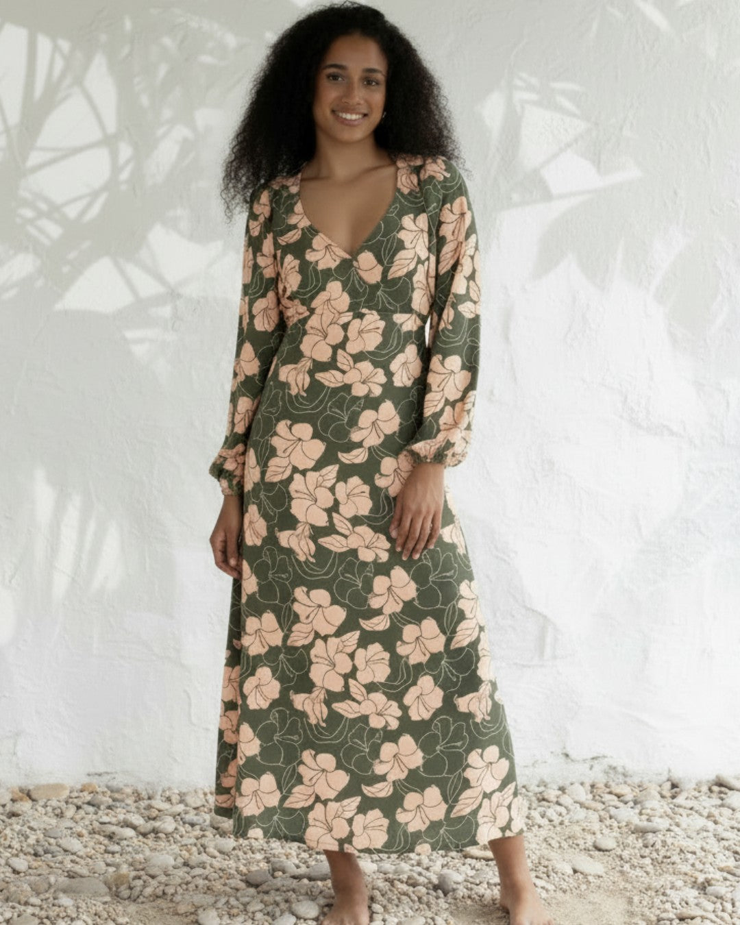 Woman wearing a floral dress standing on pebbles with a white textured background
