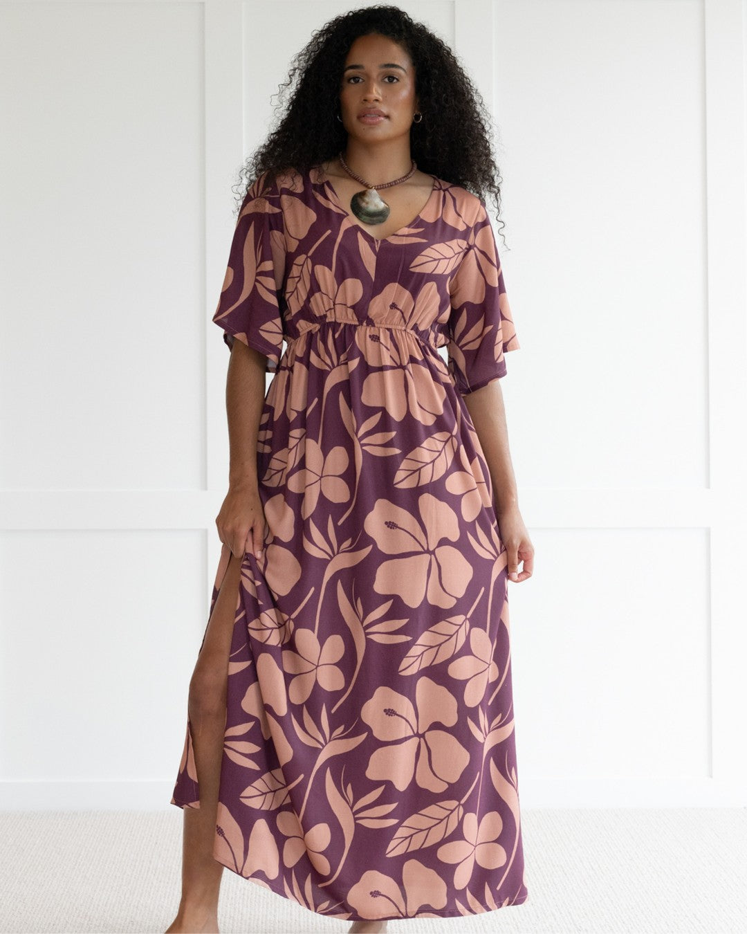 Woman wearing a purple floral island dress with a white background