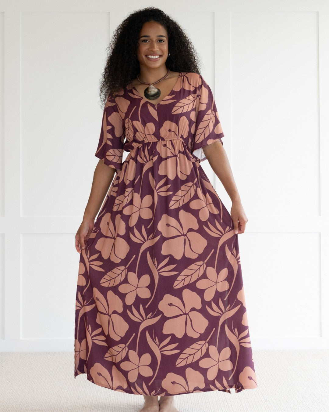 Woman wearing a purple floral island dress with a white background