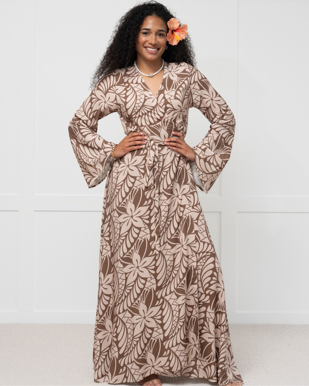 Woman wearing a long brown floral island dress against a white background