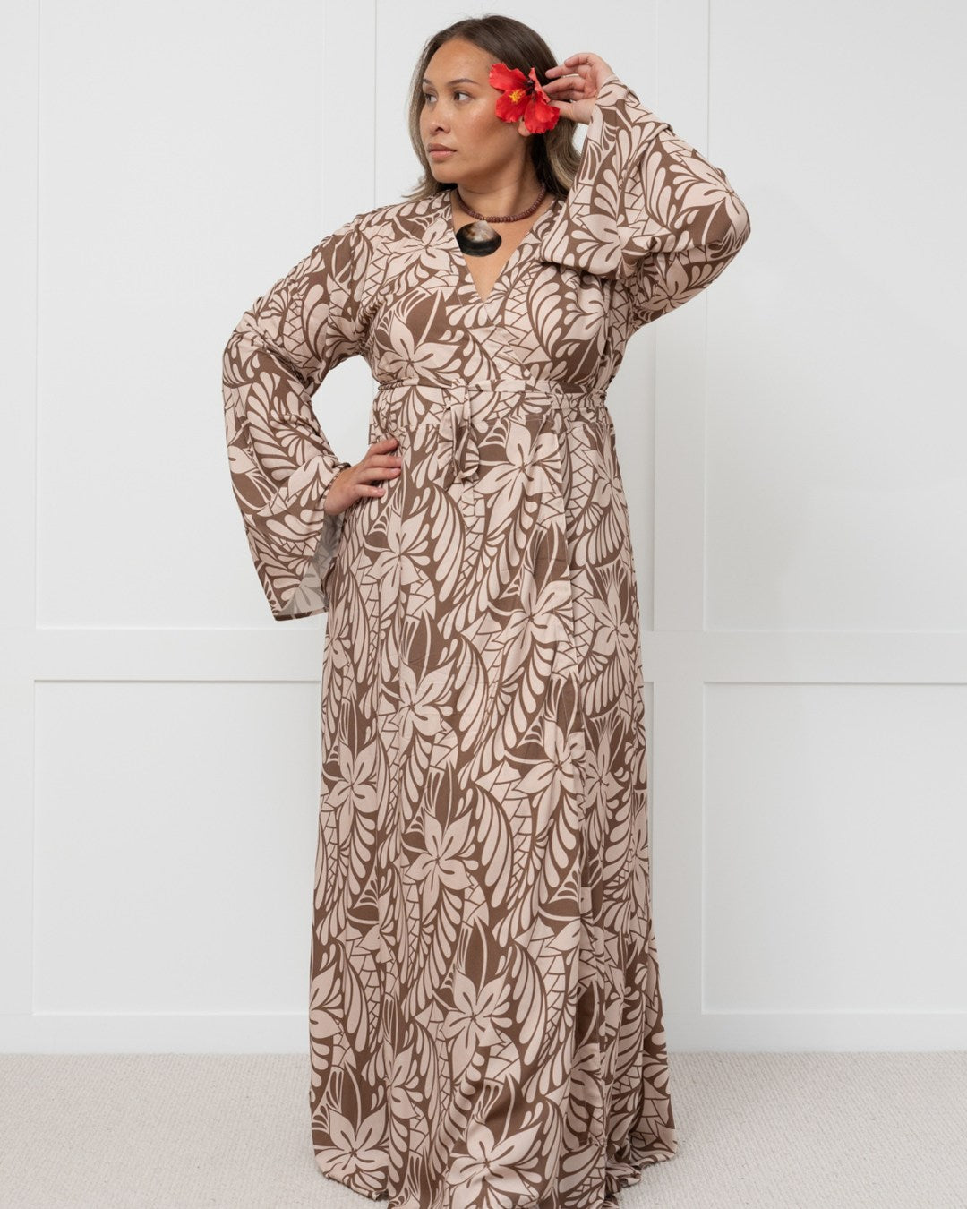 Woman wearing a long brown floral island dress against a white background