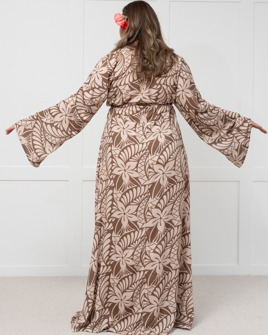 Woman wearing a long brown floral island dress against a white background