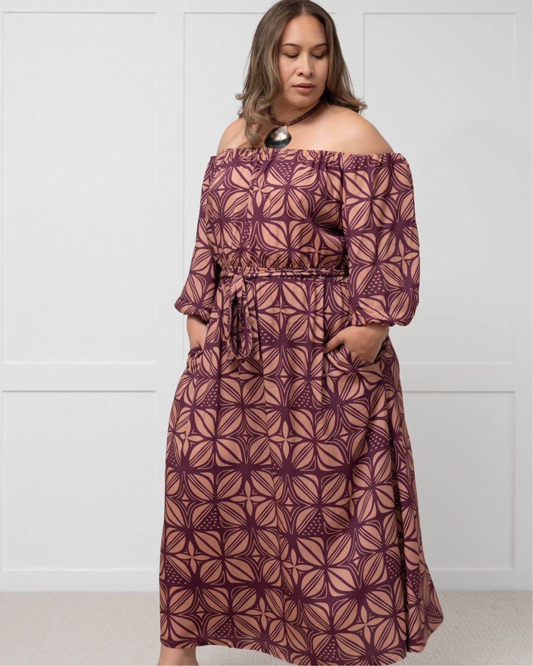 Woman wearing a patterned island dress against a white wall