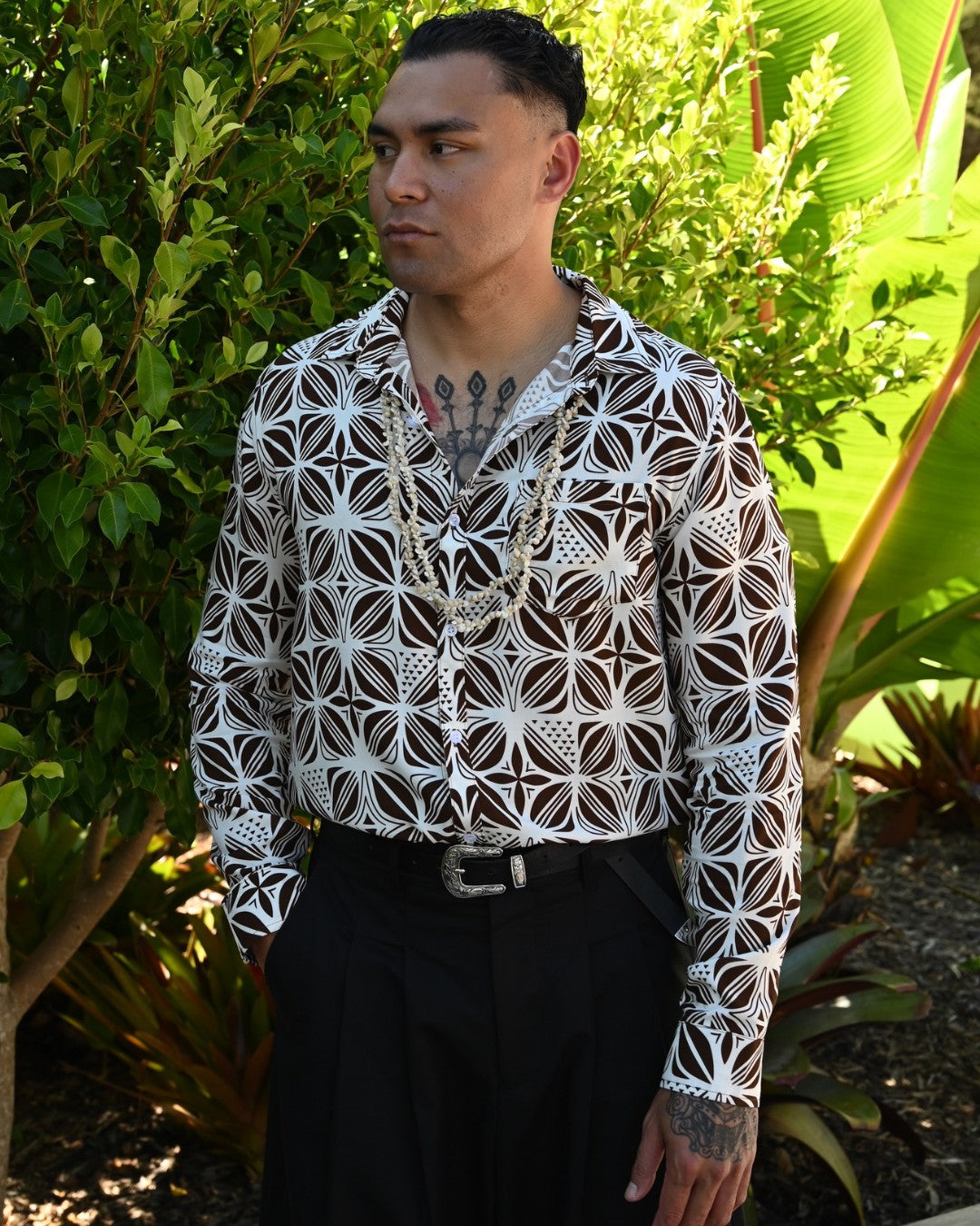Man wearing a patterned island shirt and black pants standing in a garden